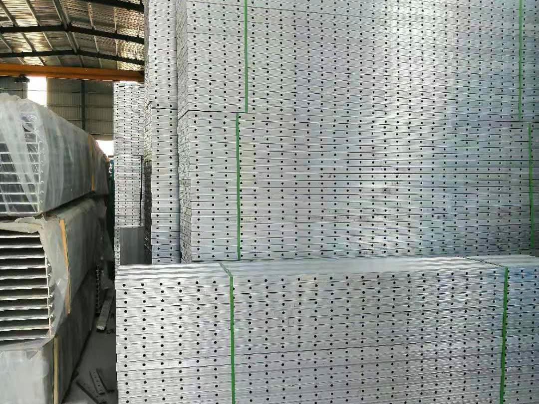 Tall strapped stacks of perforated silver aluminium sections in a warehouse.