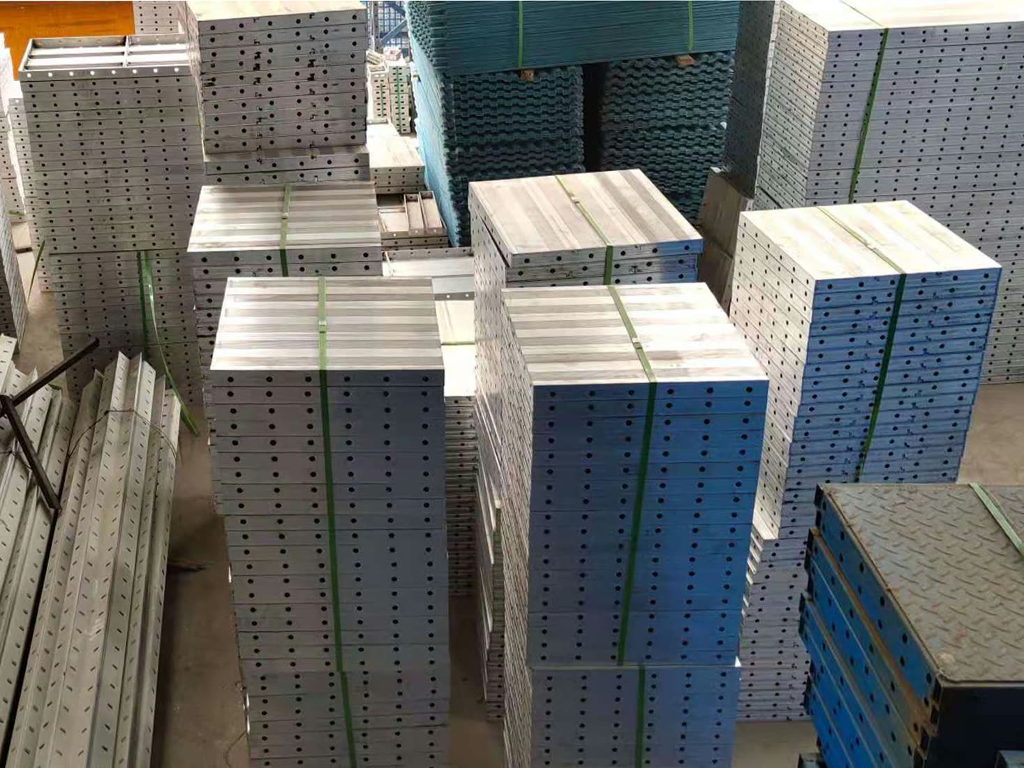 Strapped stacks of perforated aluminium panels and channels, with blue steel components topped with chequer plate in the foreground.